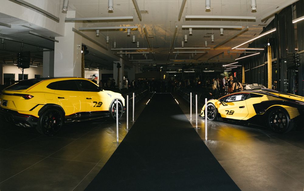 Two yellow luxury sports cars parked in a dimly lit indoor showroom with sleek black flooring and modern lighting.