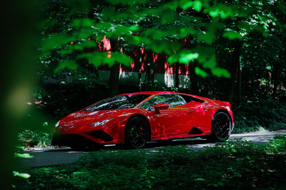 A red Ferrari sports car crashed and damaged in a wooded area during daytime.