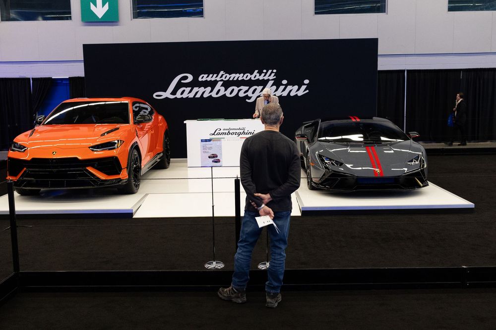 Orange and black performance cars on display at an auto show with visitors viewing the exhibition.