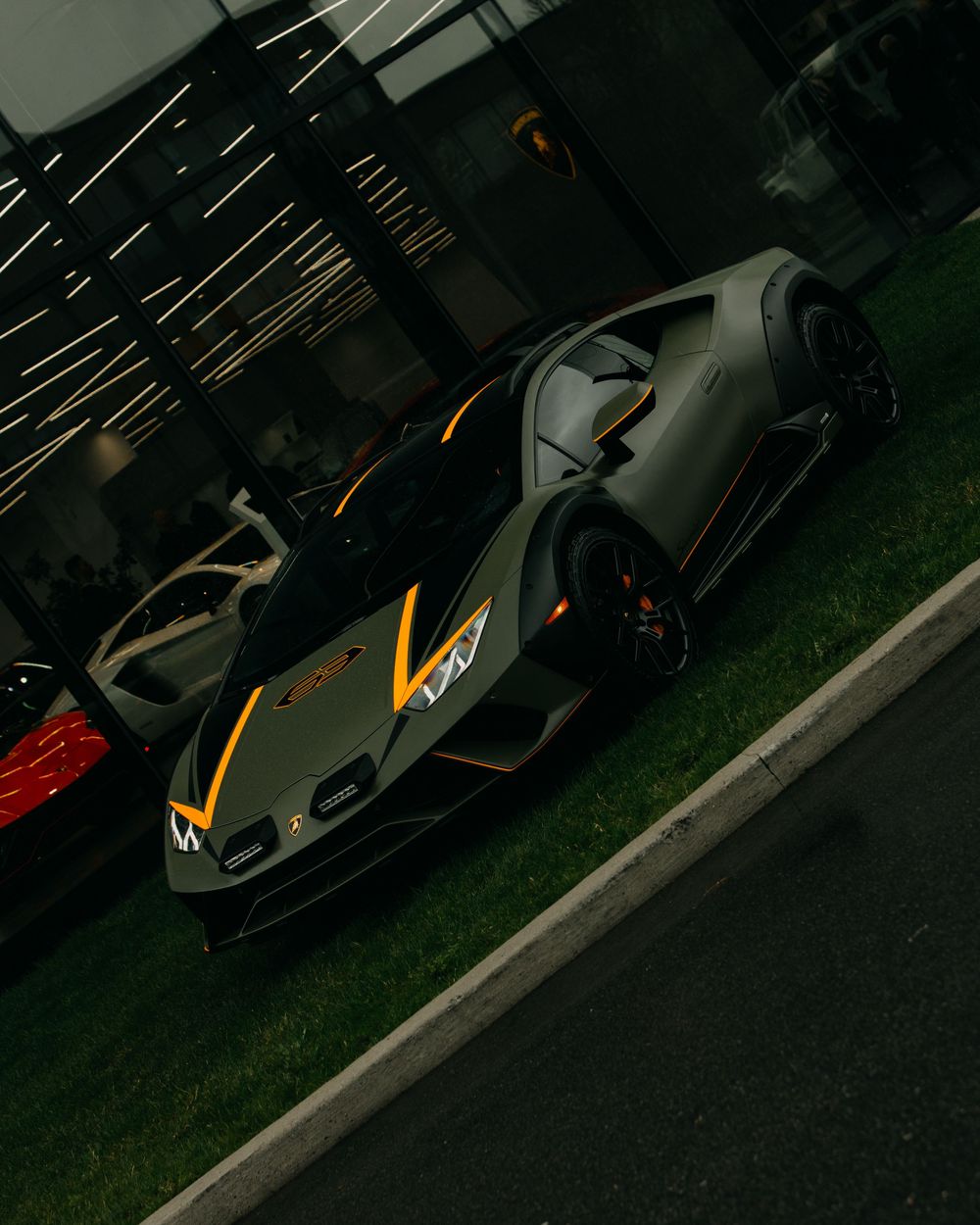High-performance Lamborghini sports car in matte gray with orange accents parked on grass under dramatic lighting.