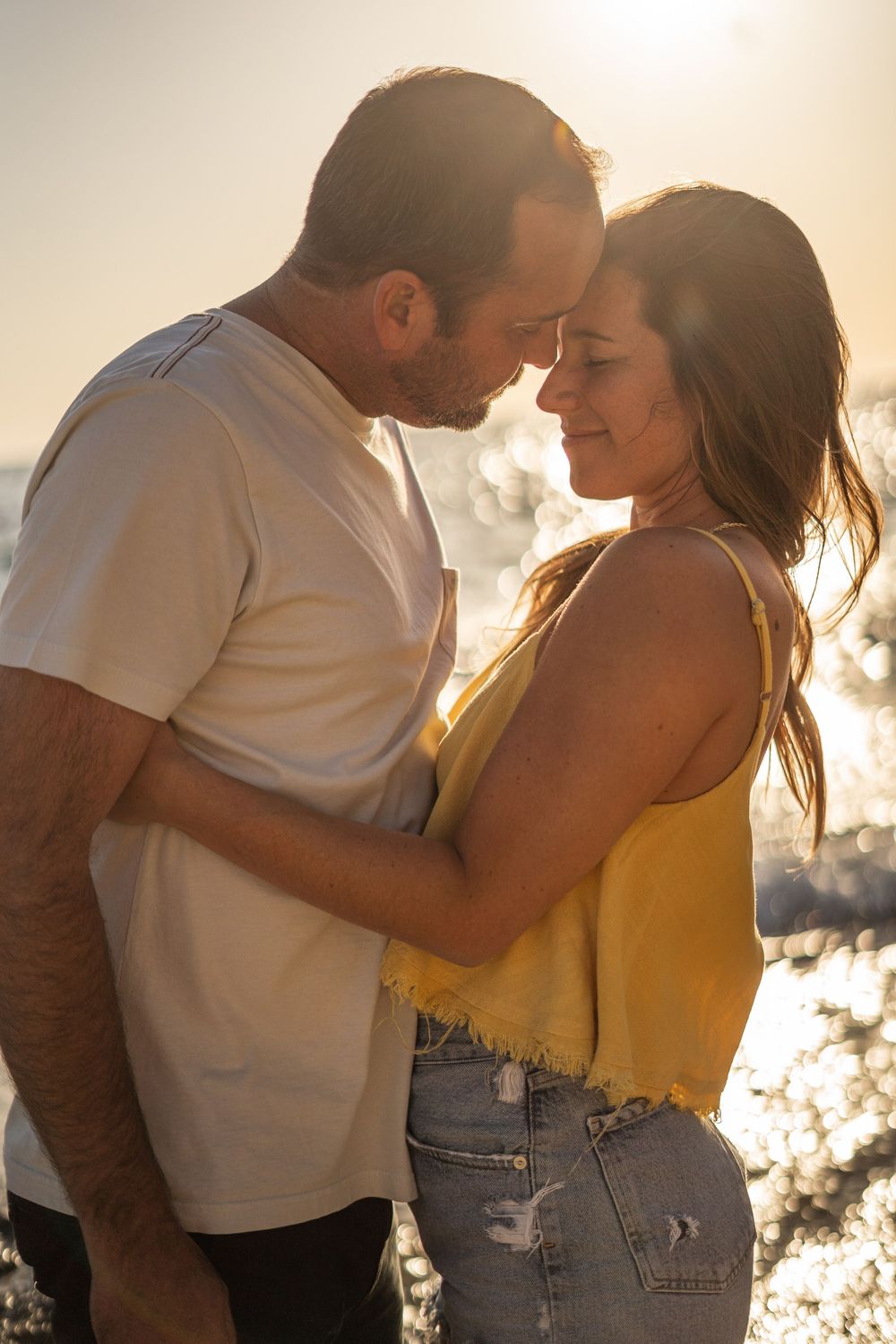 A couple embraces intimately against a golden sunset backdrop, creating a romantic silhouette effect.