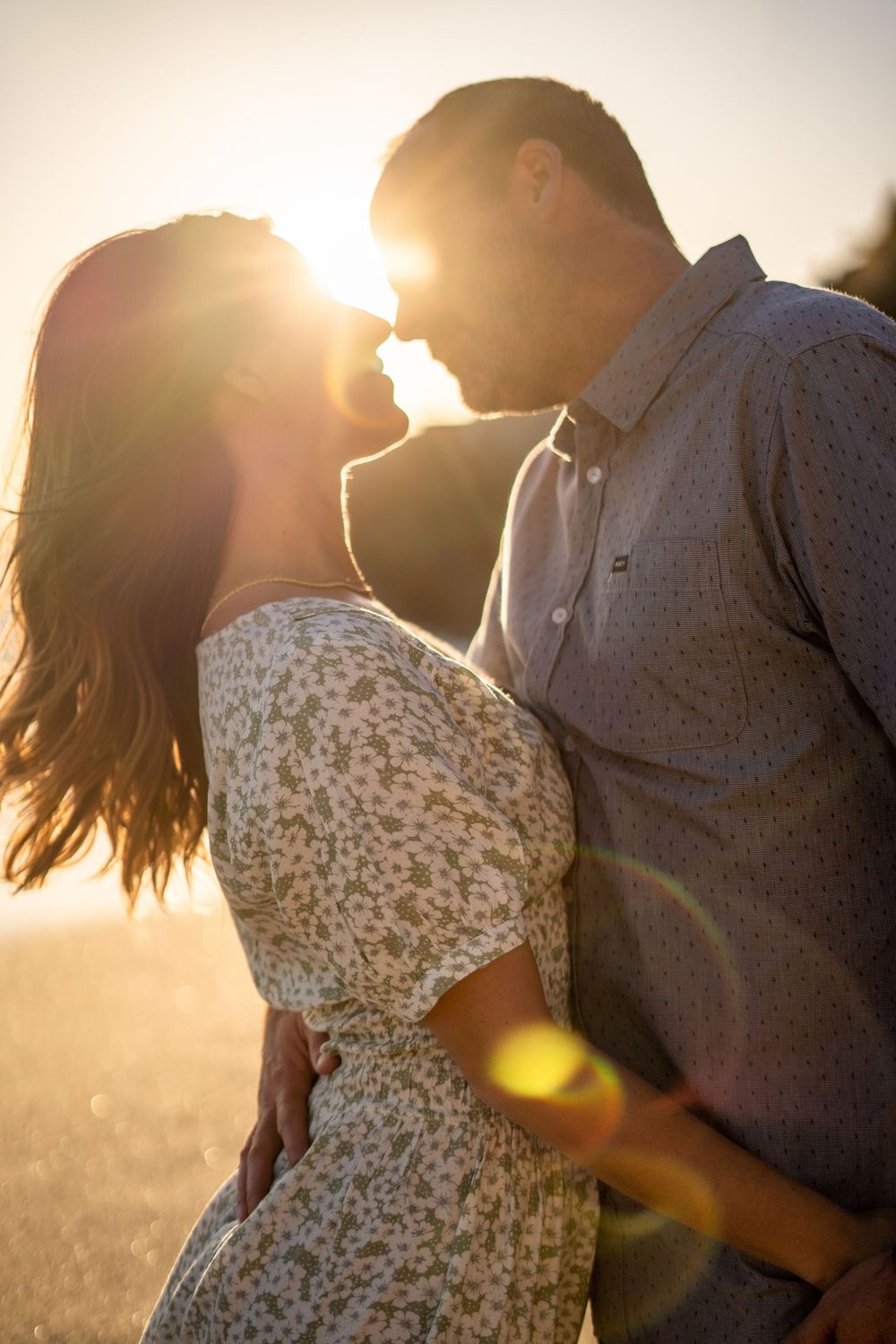 A romantic couple embraces in a sun-drenched field during golden hour as sunflares dance across the frame.