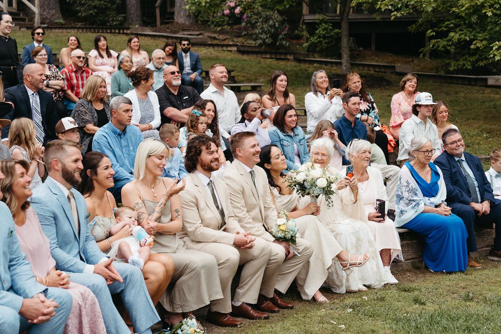 Wedding guests seated on grass watching an outdoor ceremony.