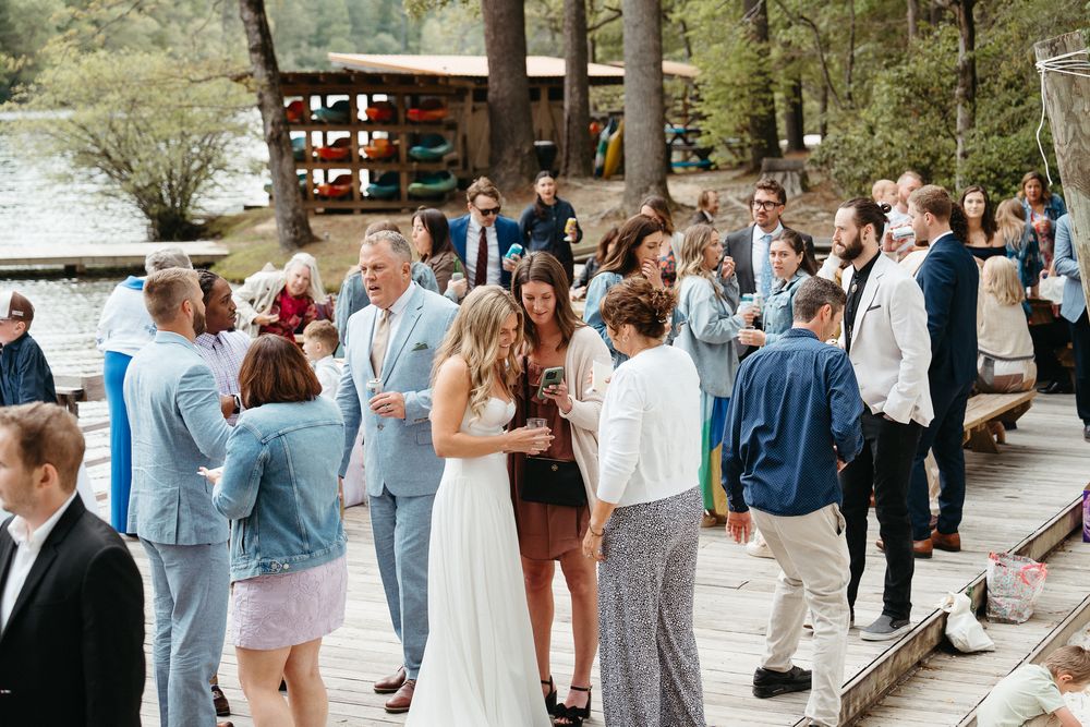 Wedding guests mingle and socialize at an outdoor reception venue surrounded by trees and natural scenery.