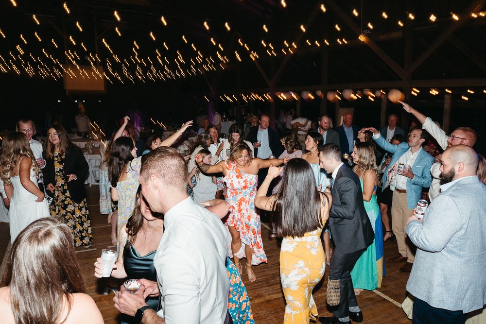 Wedding guests dance and celebrate on a dimly lit dance floor with string lights overhead. Hendersonville, NC Wedding Photographer