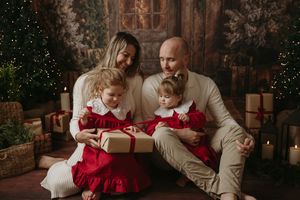 A family sits together on a couch during Christmas time with holiday decor and lights in the background.