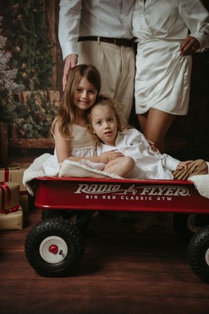 Four connected photos showing a classic red Radio Flyer wagon and white-dressed figures in a vintage-style indoor setting.