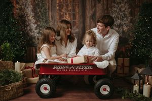 A family sits together in a red Radio Flyer wagon during a cozy outdoor holiday photo session.
