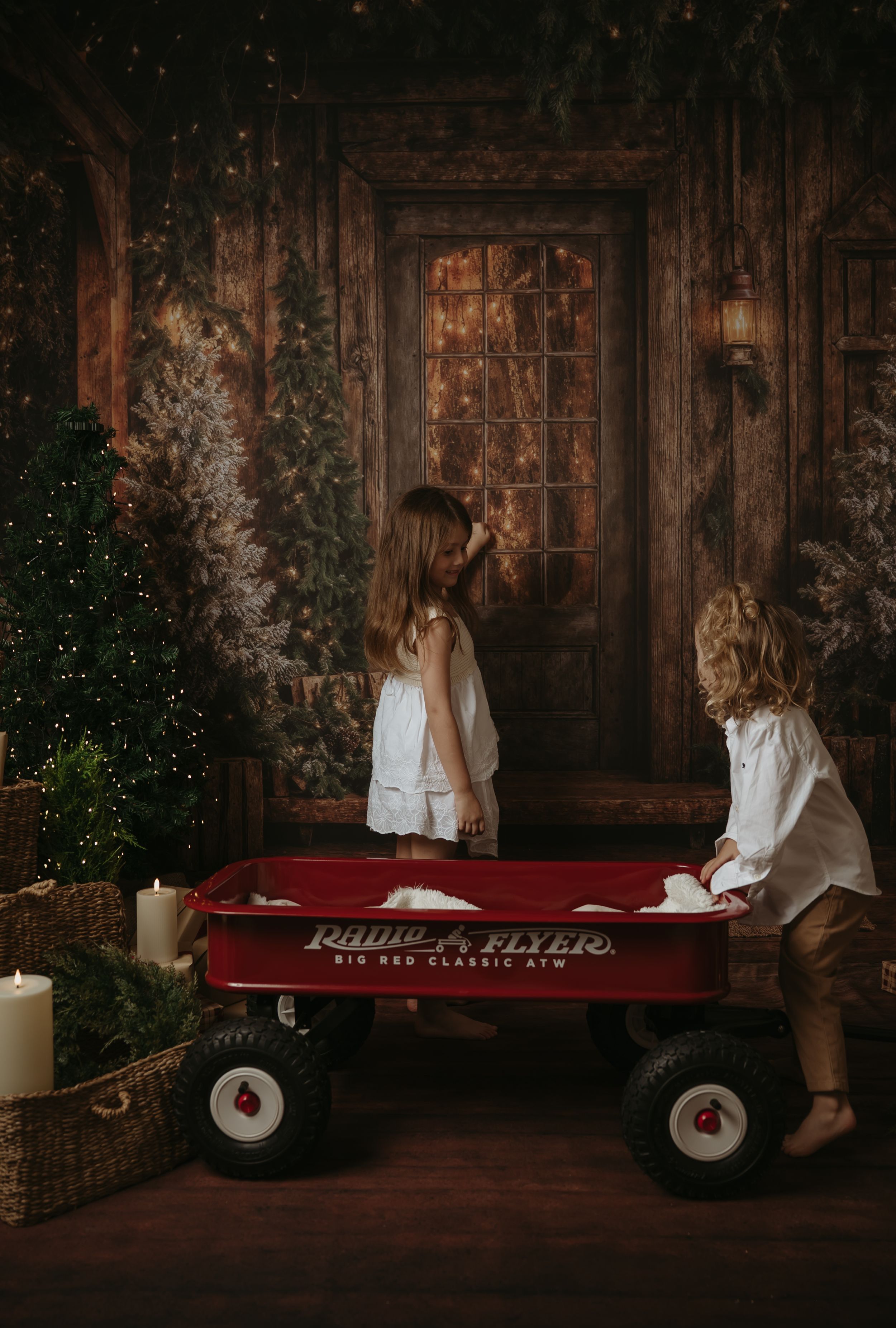 Moody holiday scene with a vintage red Radio Flyer wagon decorated with Christmas trees and lights against rustic wood.