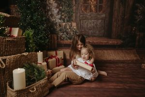 Cozy Christmas scene with white candles, wrapped presents, and rustic decorative elements arranged near a stone wall.