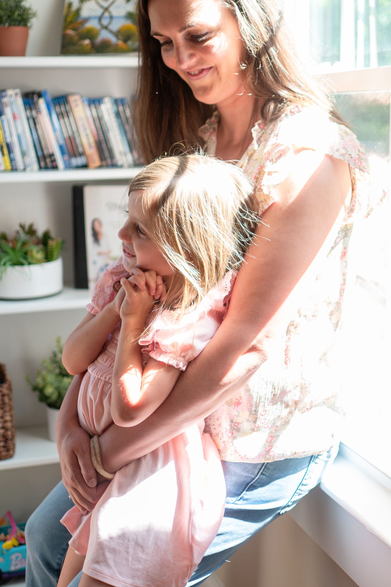 A tender moment of breastfeeding in a bright, sunlit room with bookshelves and natural decor in the background.