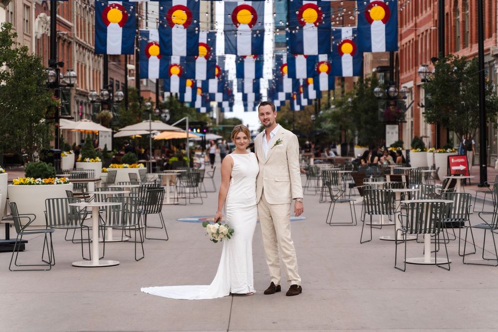 Couple walks through an outdoor venue decorated with orange lanterns and metal chairs for a wedding celebration.
