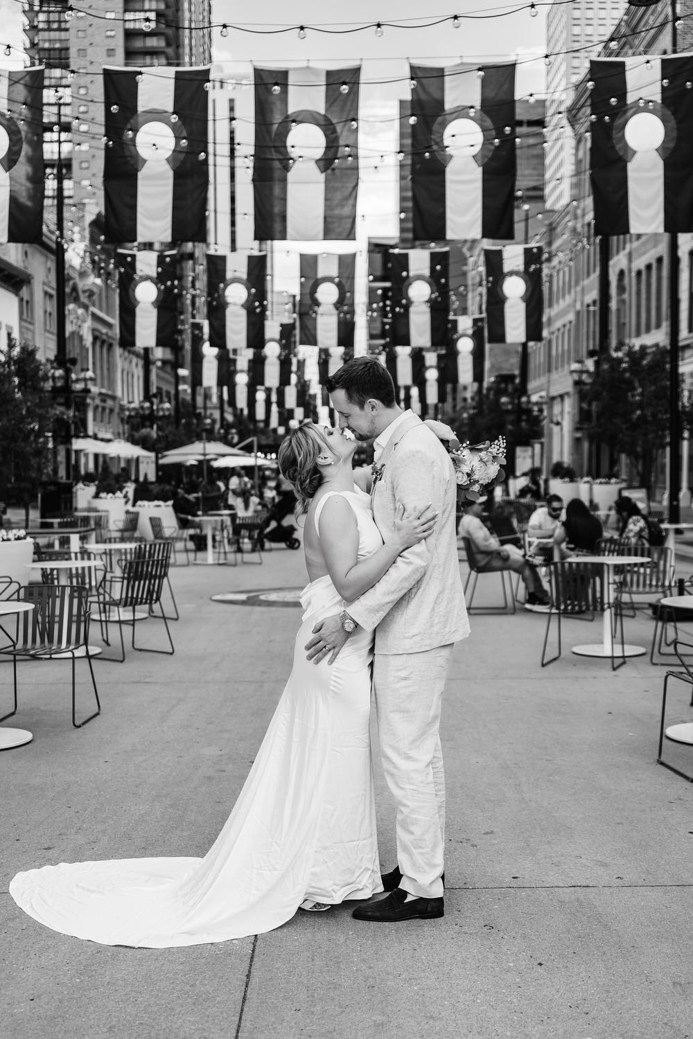 A romantic wedding couple embraces on a city street decorated with hanging white lanterns and string lights.