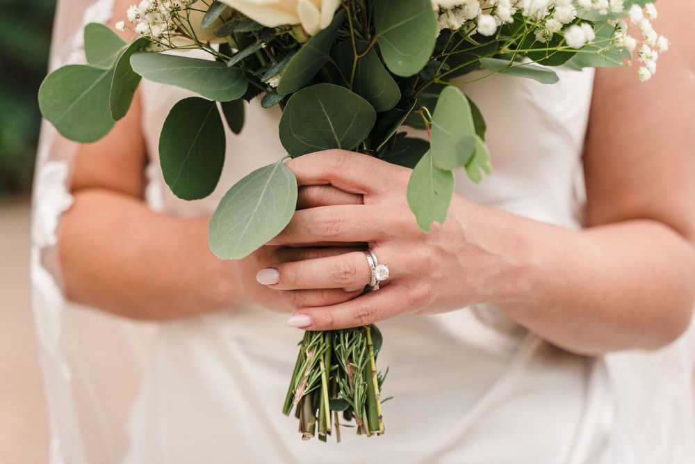 A close-up view of a bridal bouquet with white roses and eucalyptus leaves being held against a white dress.