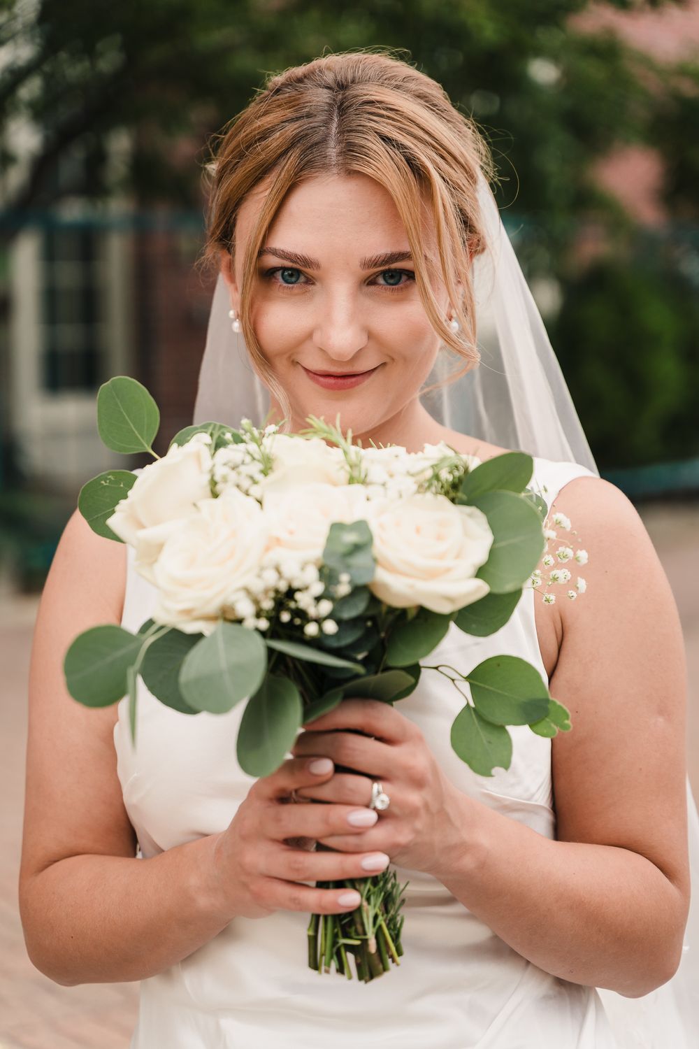 A bridal portrait showcasing a white rose and eucalyptus bouquet against a white wedding dress.