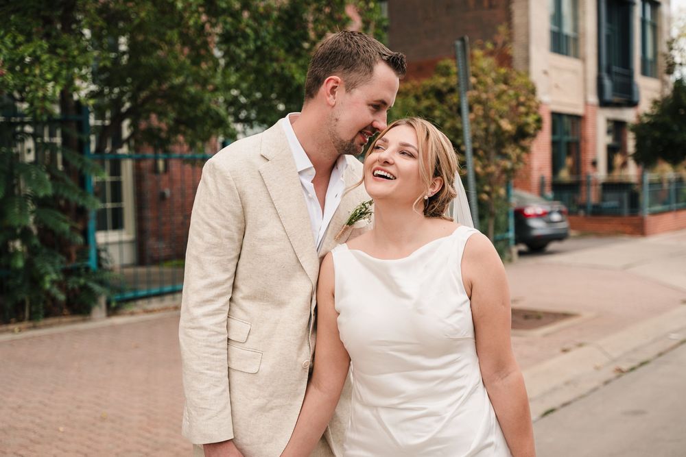 A couple in white outfits share romantic moments during a wedding photo session on a brick-lined street.