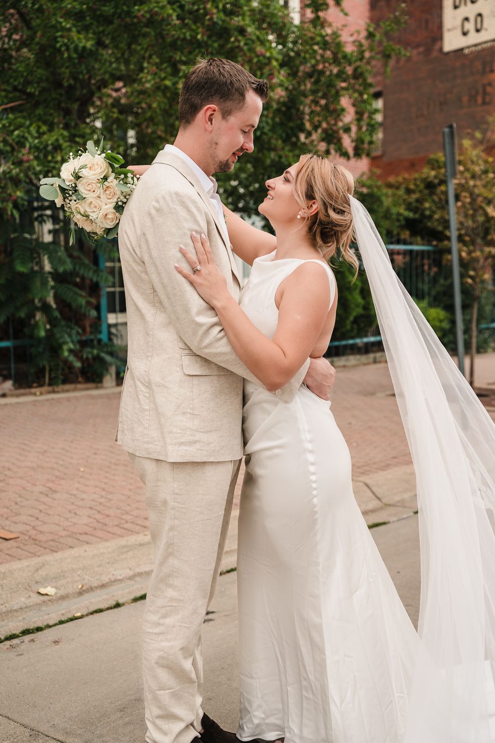 A romantic wedding moment captured on a brick sidewalk with the couple in light colored attire and a white bouquet.