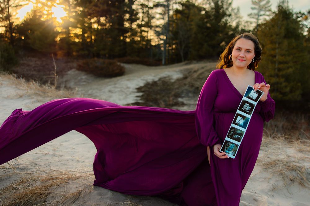 A flowing purple dress billows in the wind against a golden sunset backdrop with pine trees.