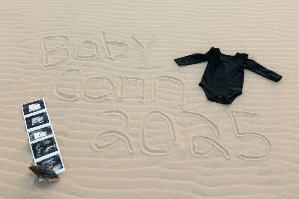 Writing in the sand on a beach shows text and symbols with a dark object visible in the corner.