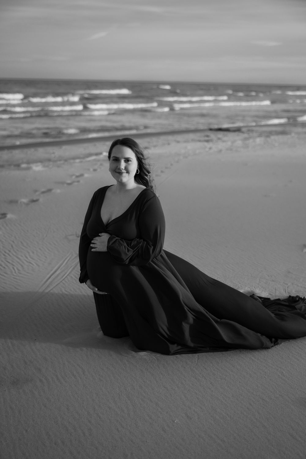 Black and white photo series of a person in dark clothing reclining on a sandy beach with ocean waves in background.