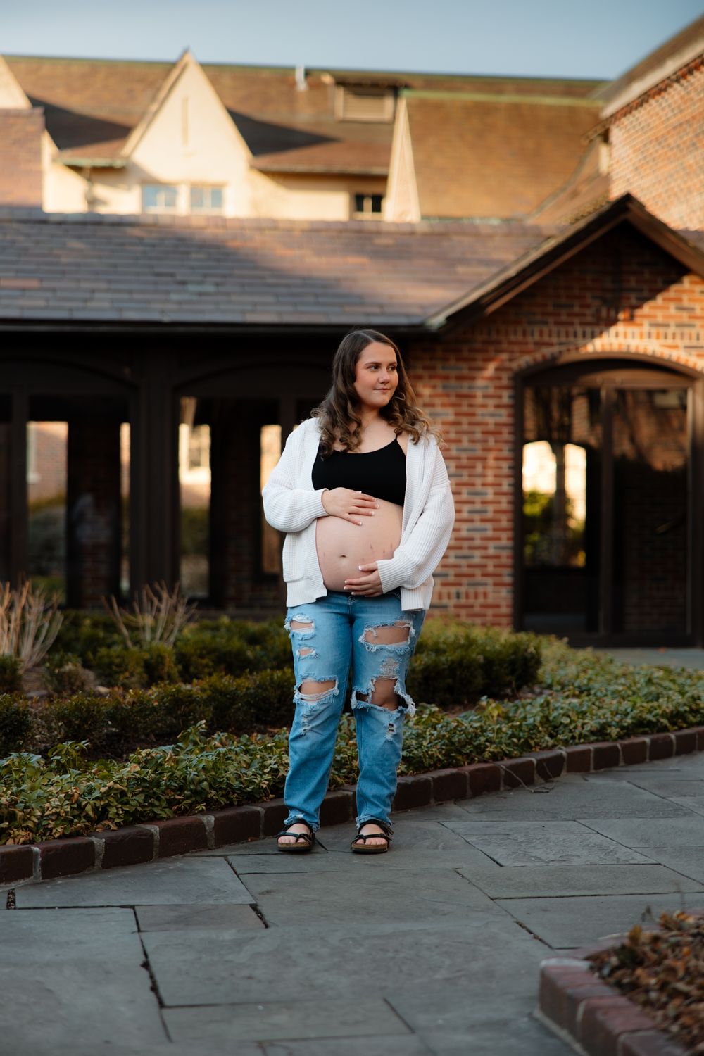 Outdoor maternity portraits on stone path with brick buildings and landscaping in background.