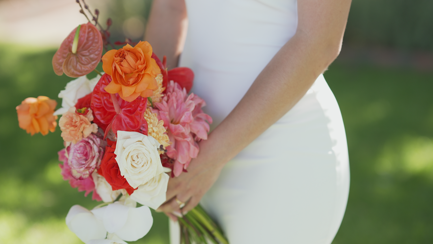 Vibrant orange and pink floral bouquet against a white dress.