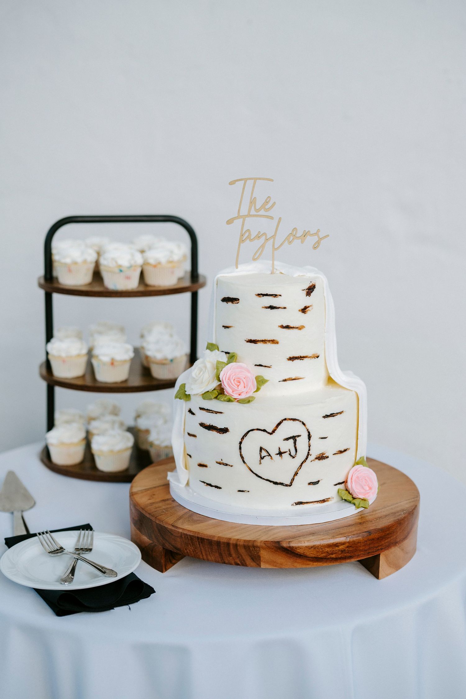 Elegant white wedding cake with delicate birch tree design and pink floral accents displayed on wooden cake stand.