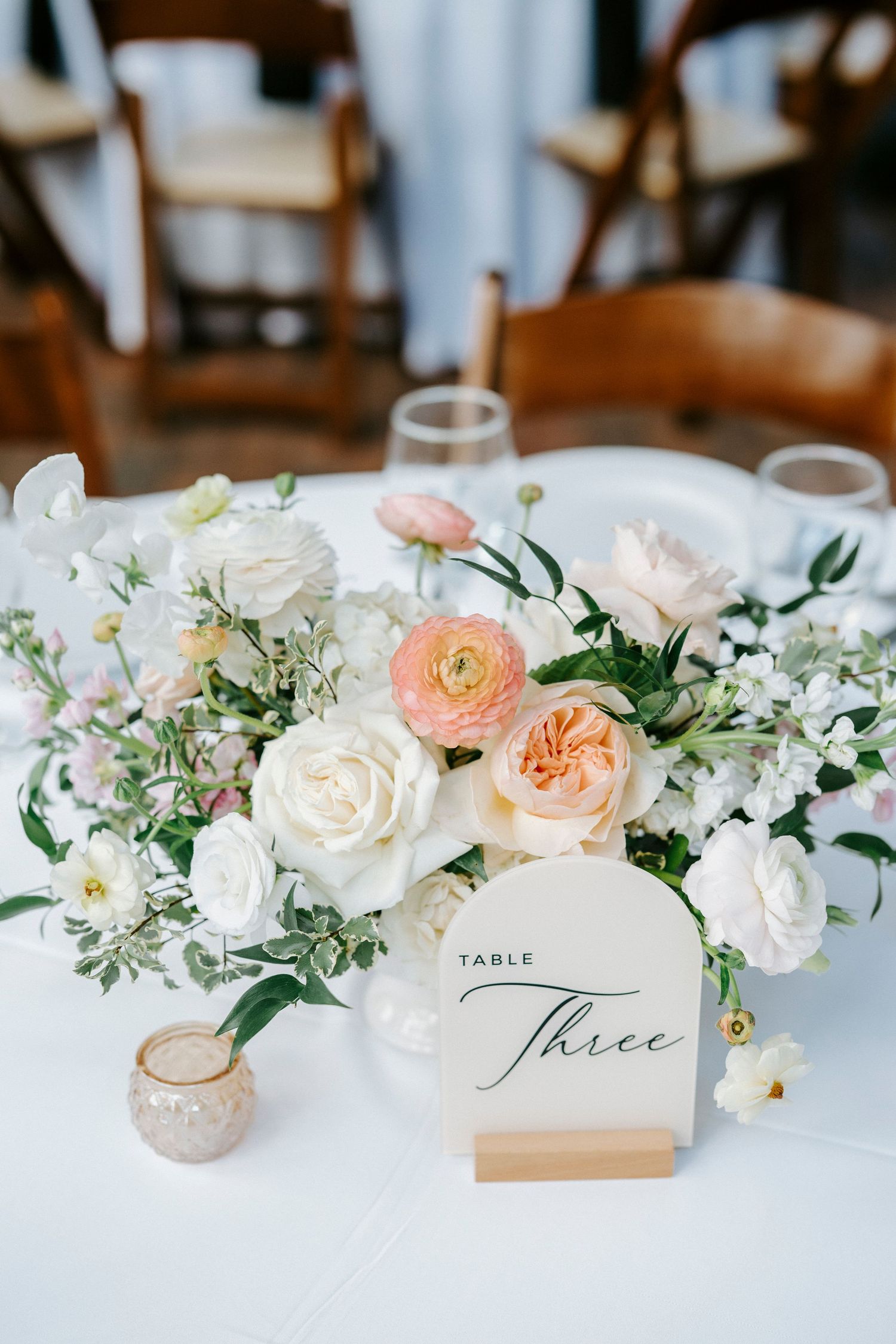 Elegant wedding table decor with peach and white floral arrangements and calligraphy table number cards.