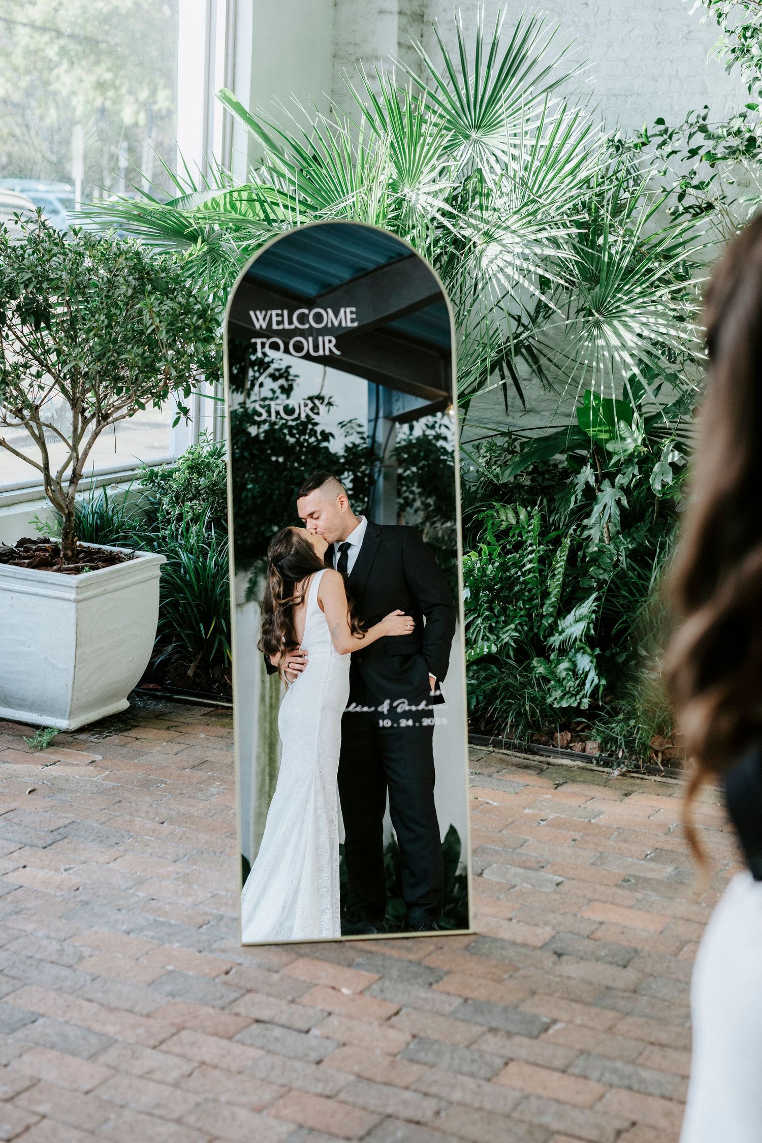 Elegant outdoor wedding ceremony setup with palm plants and a welcome sign on a brick patio.