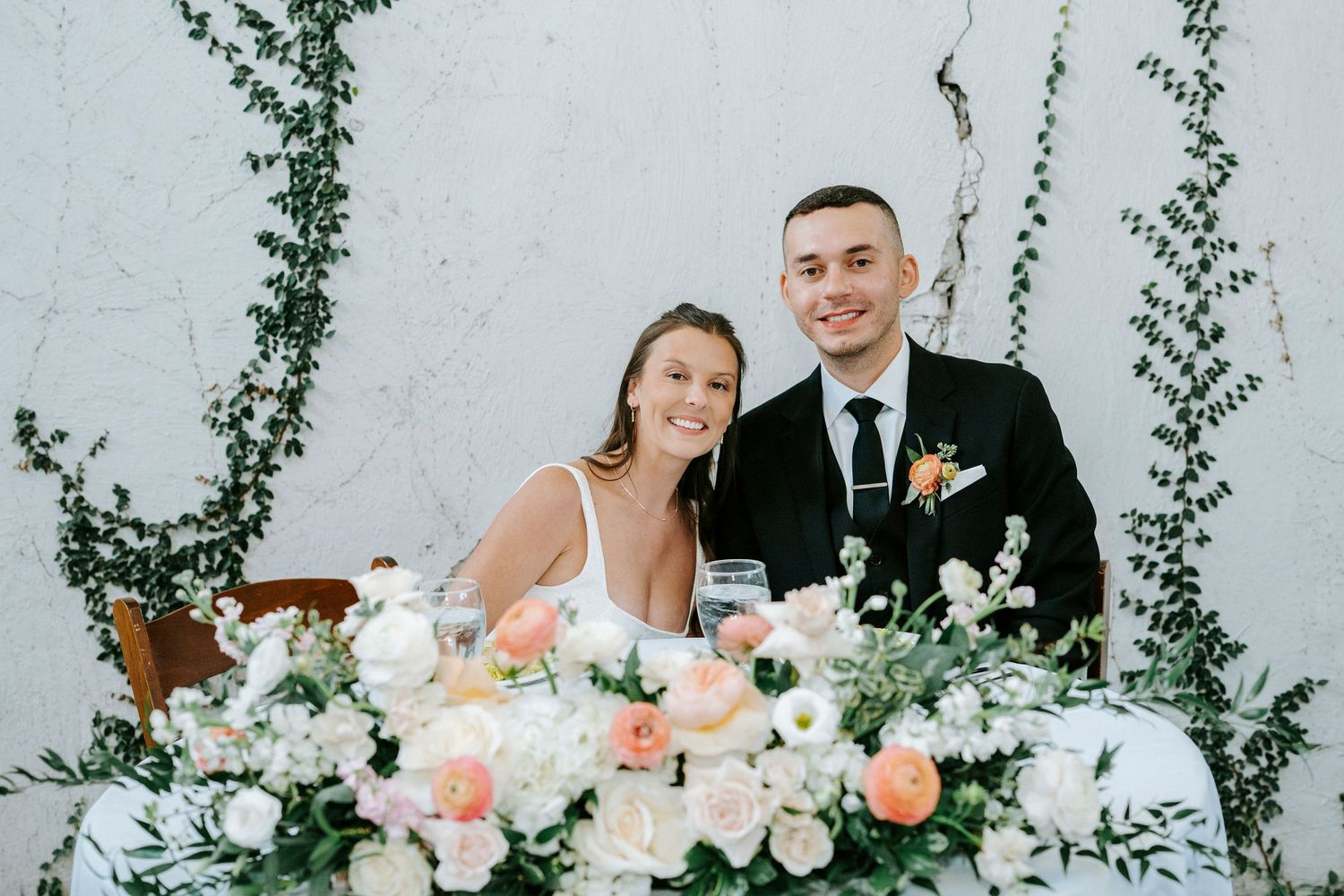Wedding couple poses outdoors with greenery and floral arrangements in a series of romantic portraits.