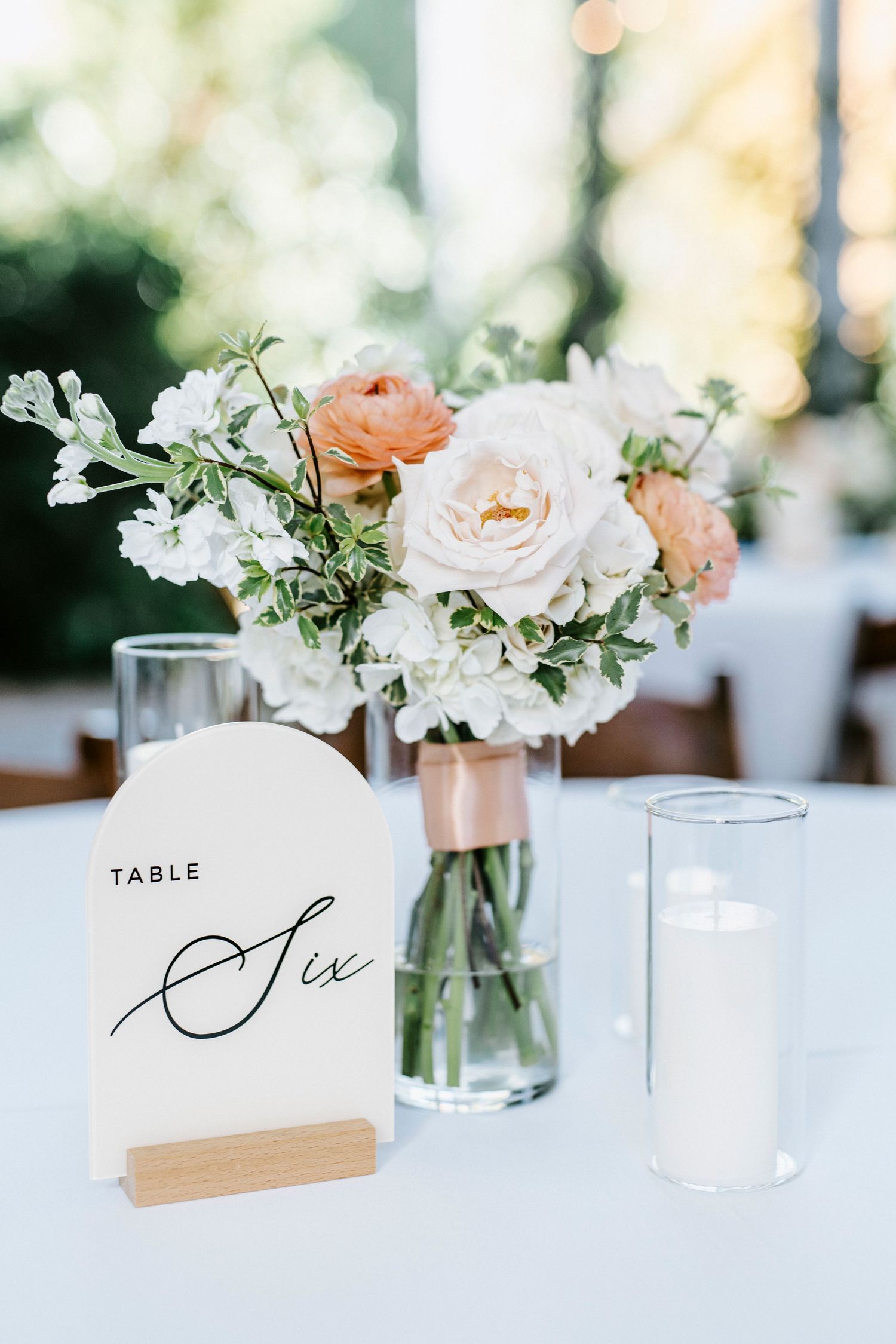 Elegant wedding table setting with white and peach floral centerpieces and handwritten table number cards.