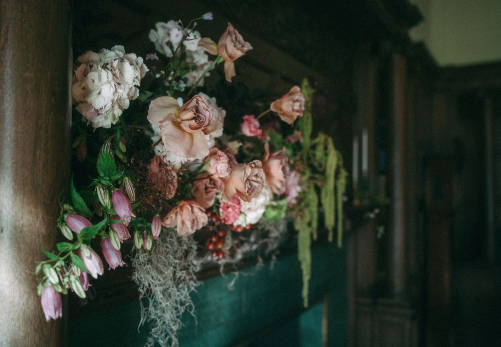 Pink and peach floral arrangements with greenery decorate a dark wooden interior space.