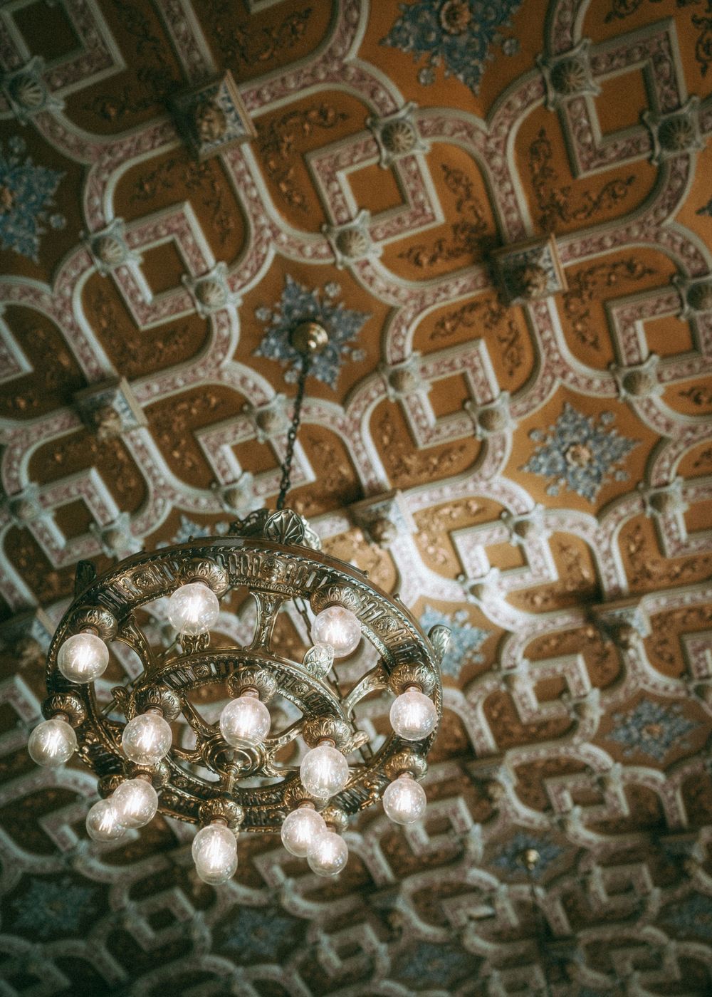 Ornate vintage ceiling with geometric patterns illuminated by elegant crystal chandeliers.