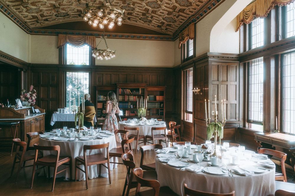 Formal dining room with wood paneling, chandeliers, and round tables set for an event.