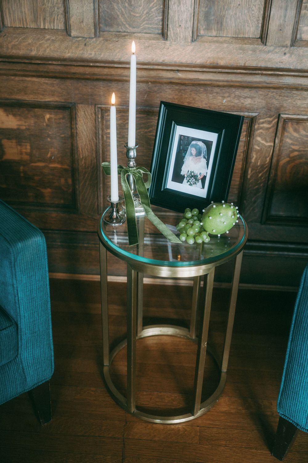 Elegant table setting with teal chairs, candlelight, and framed photos against dark wood paneling.