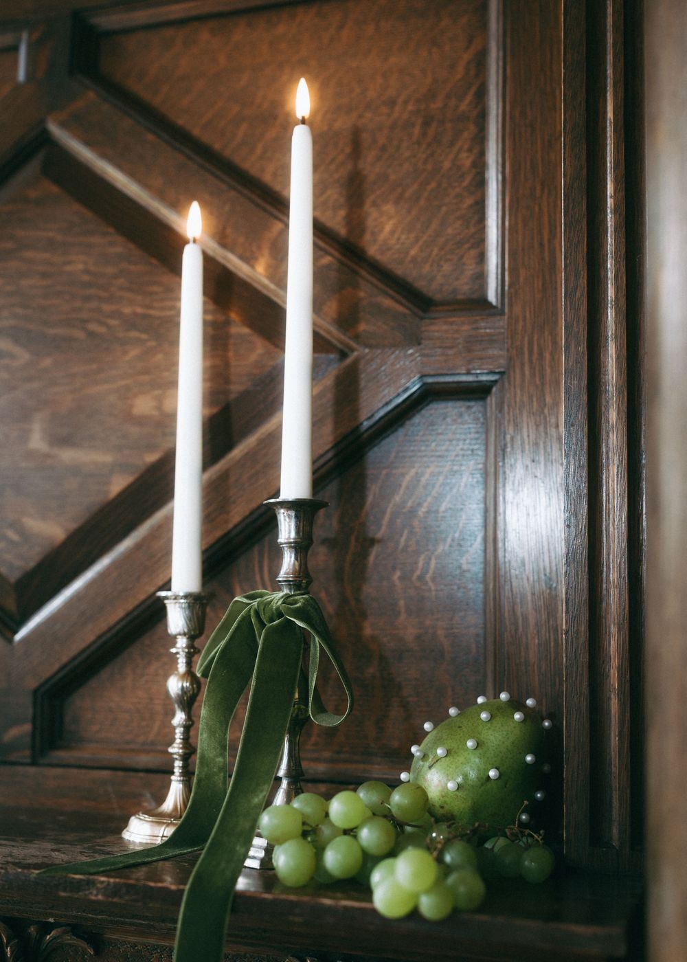 Lit white candles and green grapes arranged decoratively on dark wooden church pews.