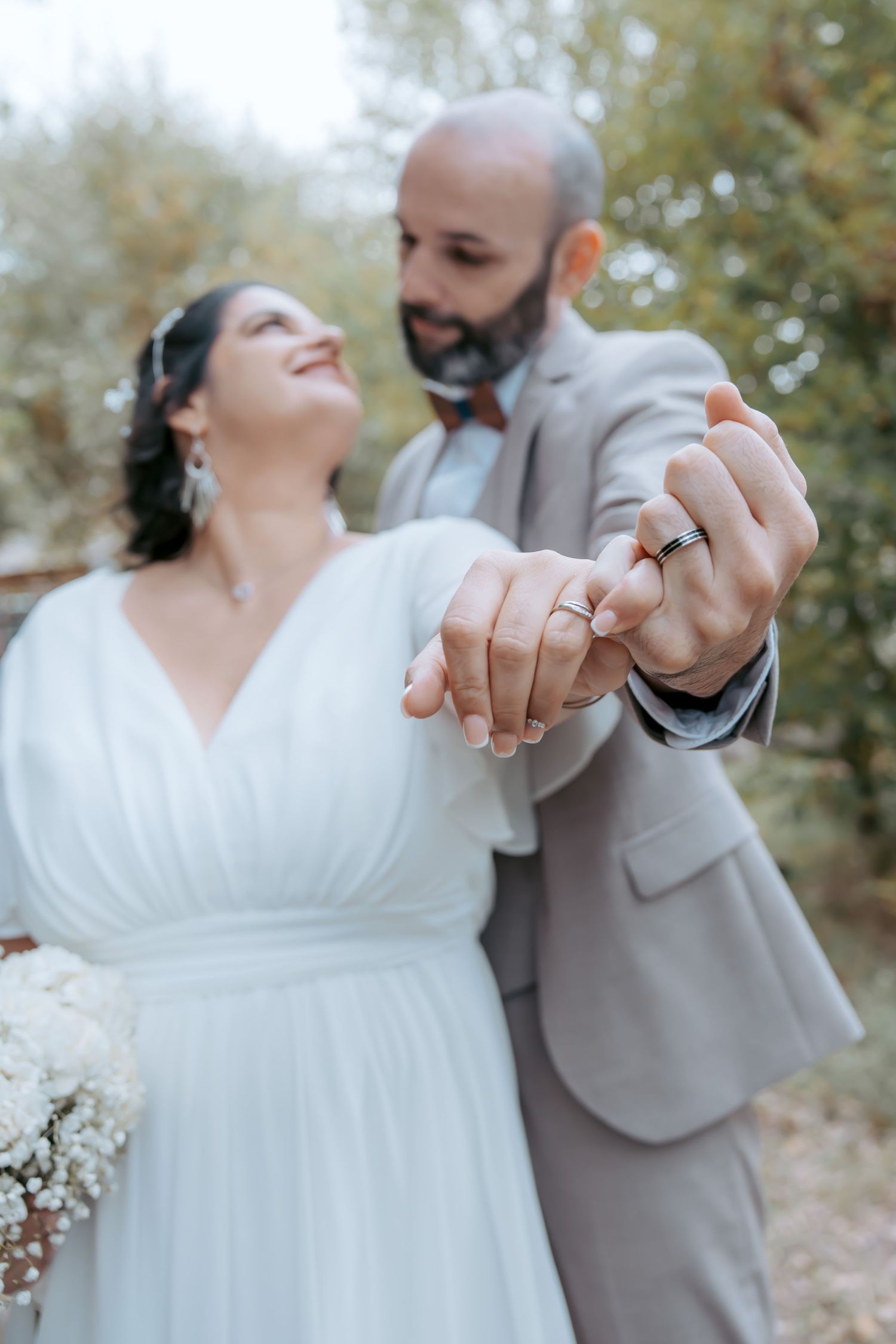A romantic outdoor wedding photoshoot showing hands with rings and white dress details.