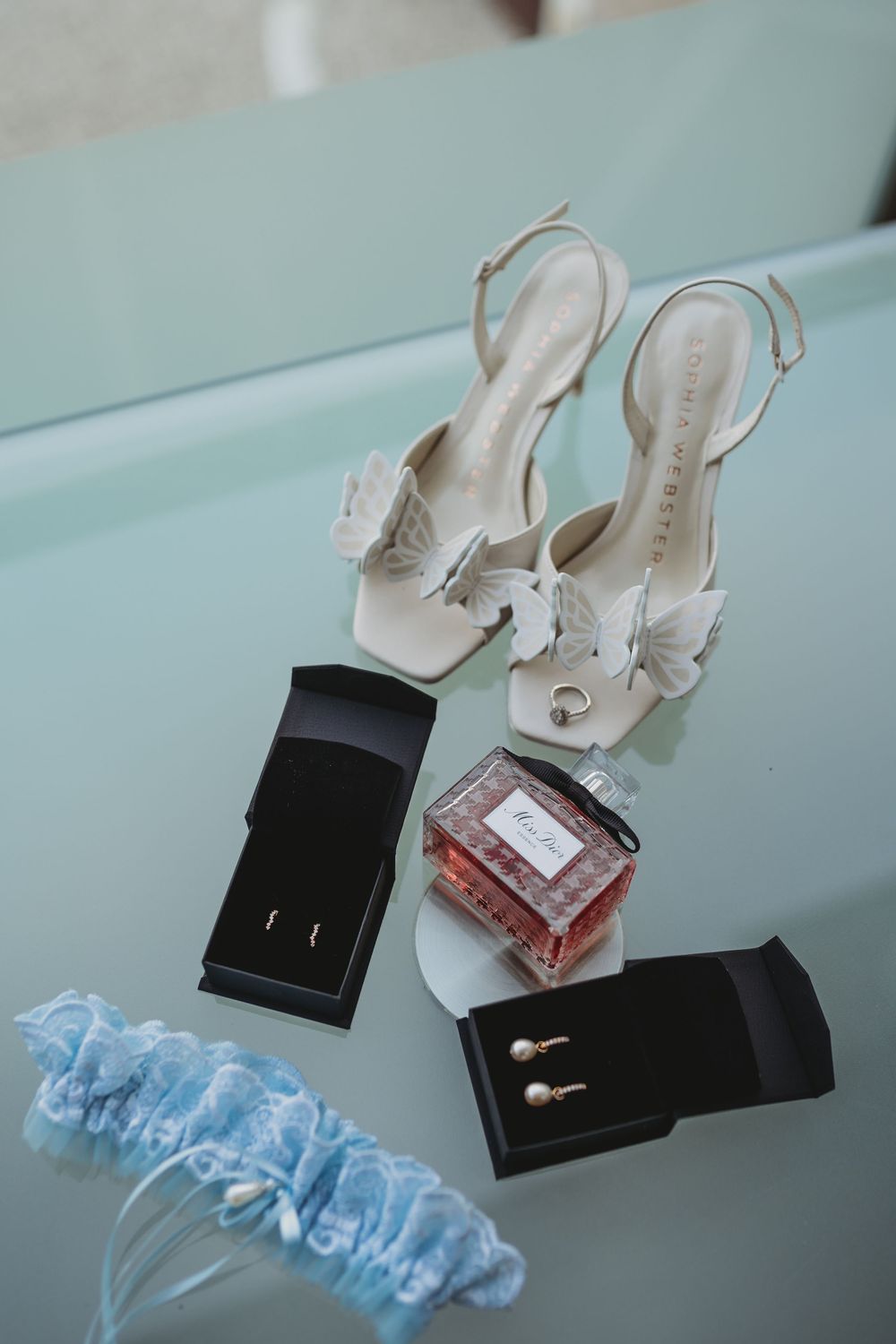 White bridal shoes and a light blue garter displayed on a light surface.