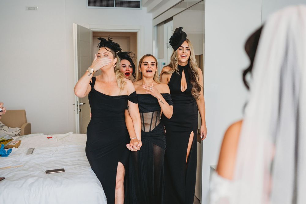 Bridesmaids in matching black dresses getting ready in a modern hotel room.