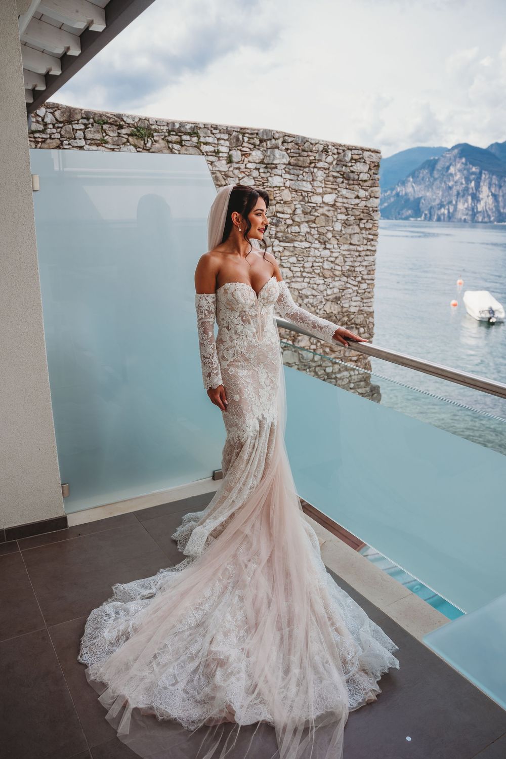 Elegant lace wedding dress with flowing train photographed against stunning Lake Como and mountain backdrop.