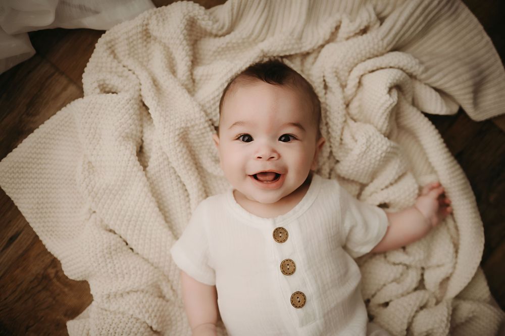 A baby wearing a white button-up outfit lies on cream-colored bedding in a series of connected photos.
