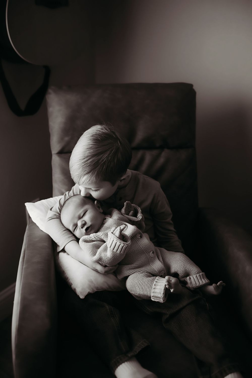 A series of intimate black and white photographs showing tender moments between sibling and sleeping newborn.