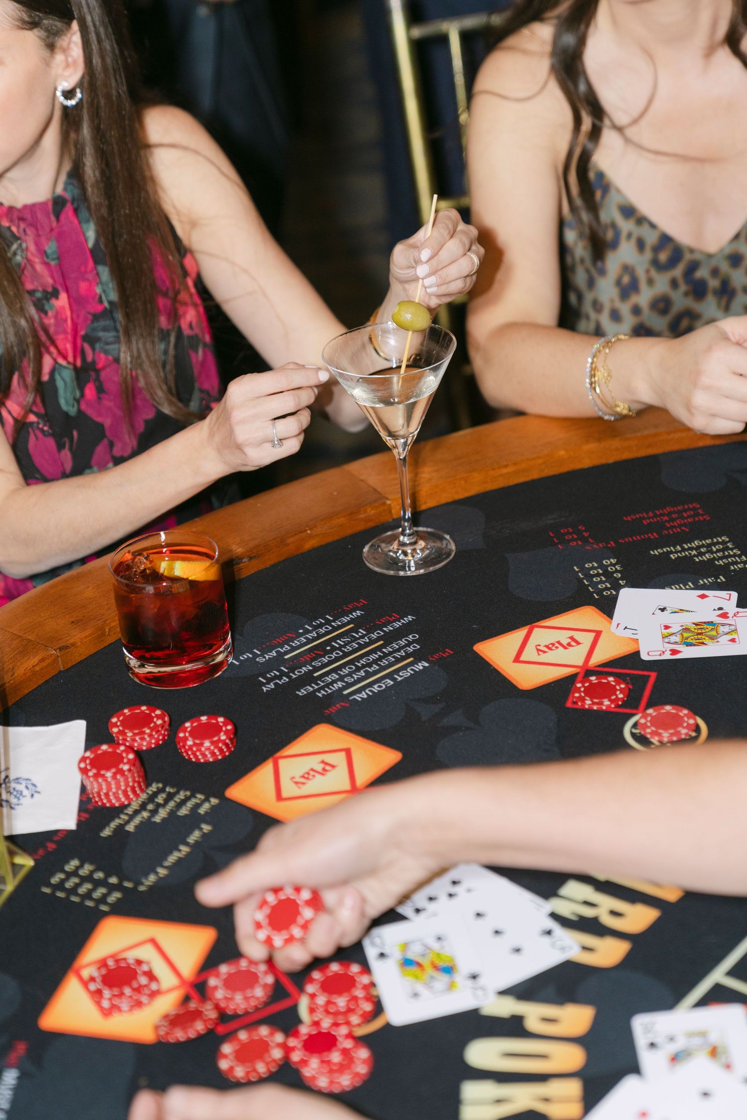 People playing poker with red casino chips and playing cards on a black table during a social gathering.