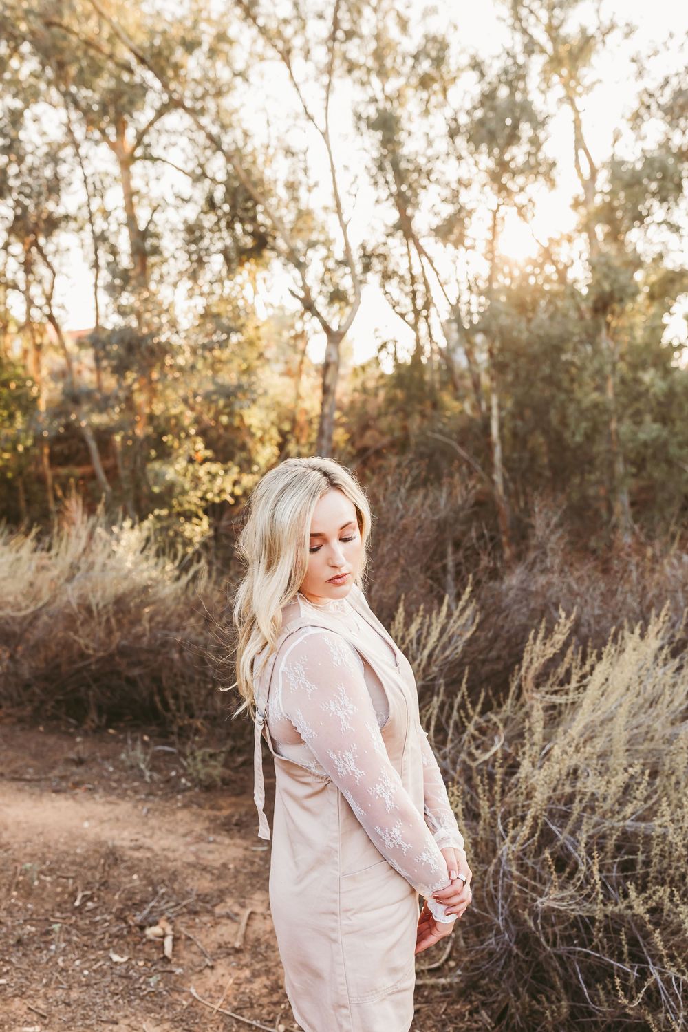 A person in a light-colored dress poses in a natural outdoor setting during golden hour.