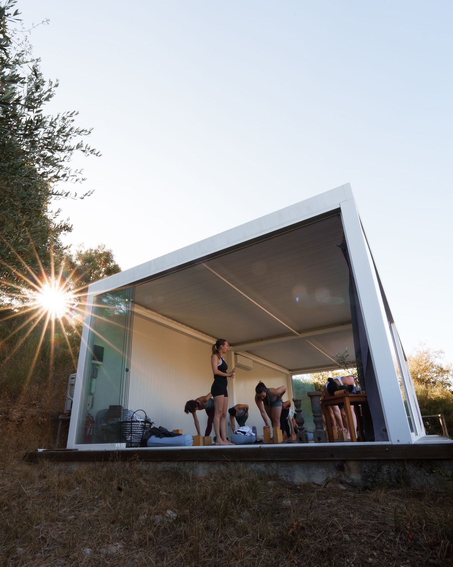 Modern white architectural structure with people gathered inside at sunset creating a dramatic silhouette against the sky.