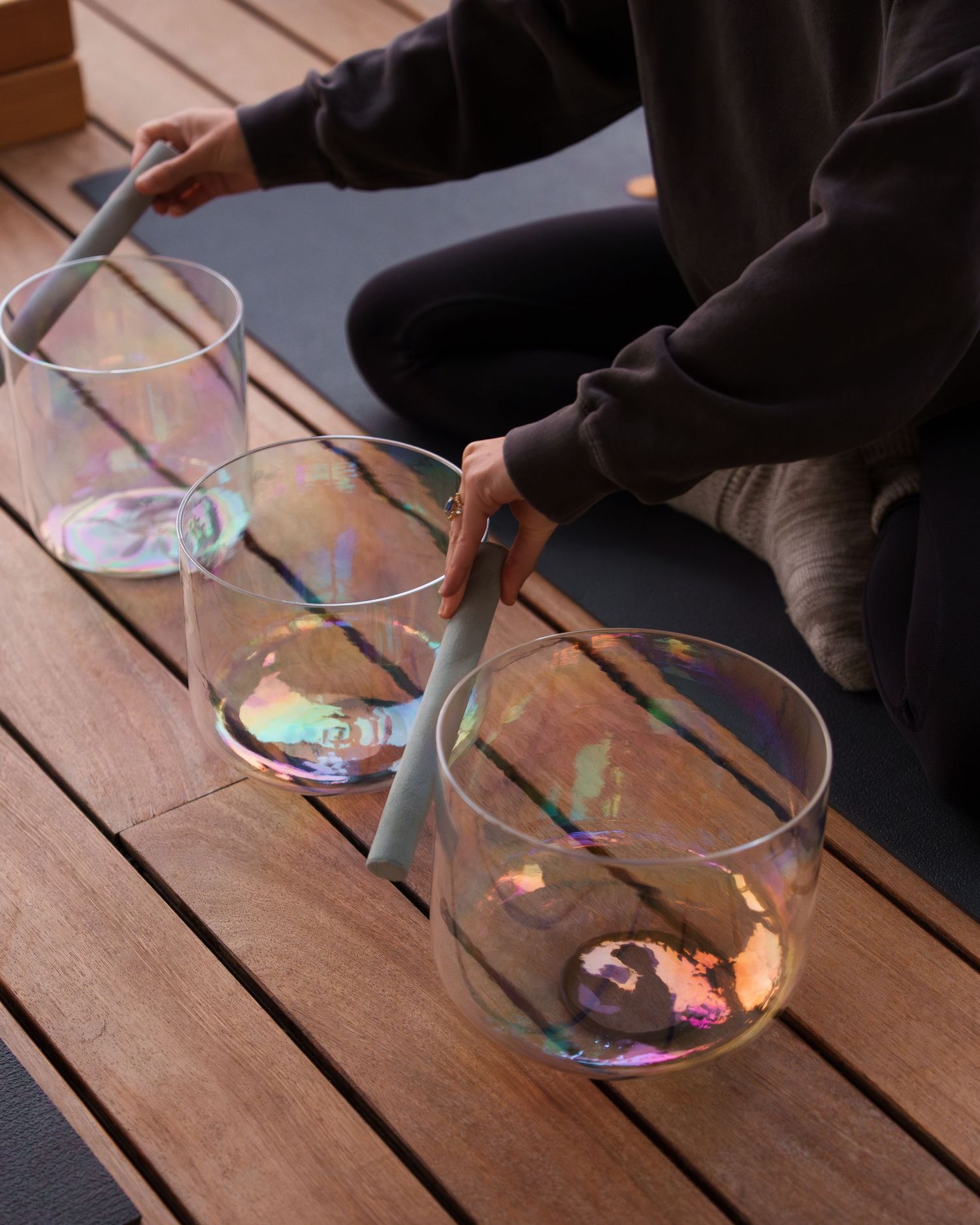Hands using chopsticks to create colorful soap bubble art on clear glass plates against a wooden surface.