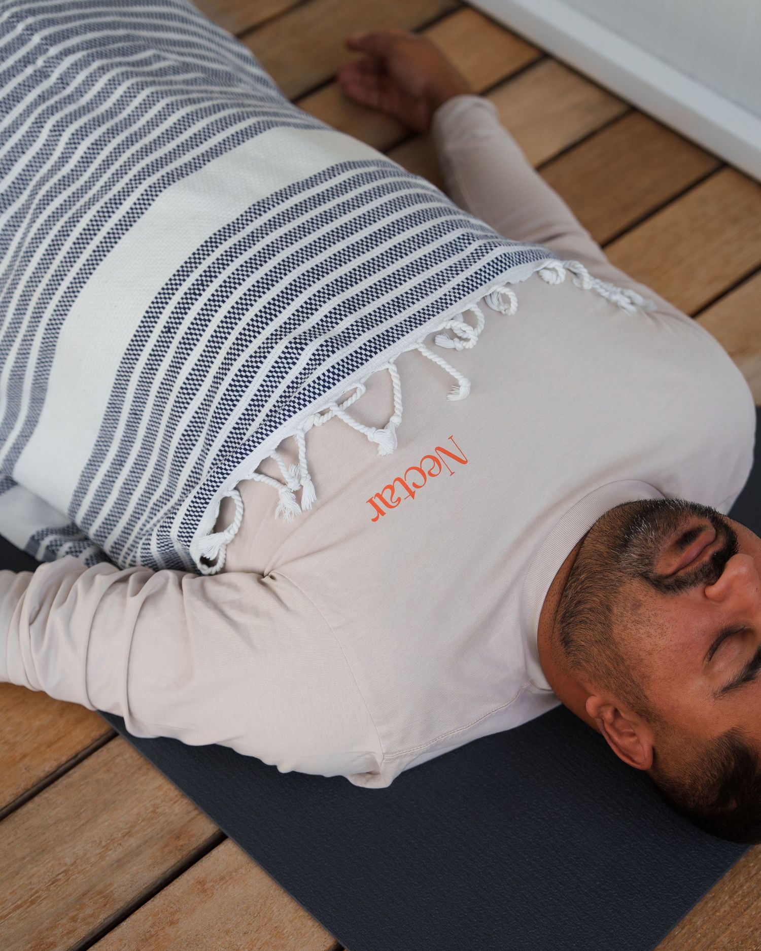 A person lying on a wooden deck with a striped pillow under their head in a relaxing pose.