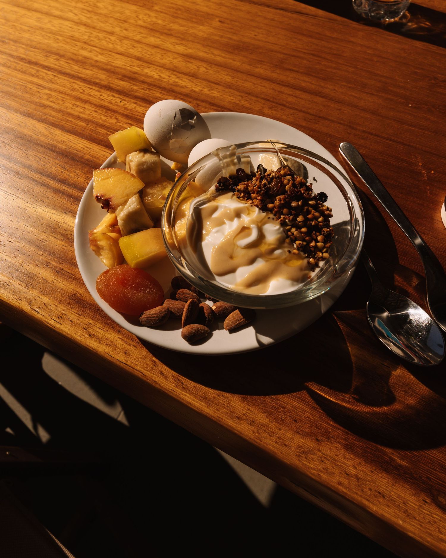 A glass bowl of vanilla ice cream topped with chocolate chips and served with fresh fruit and nuts on a wooden table.