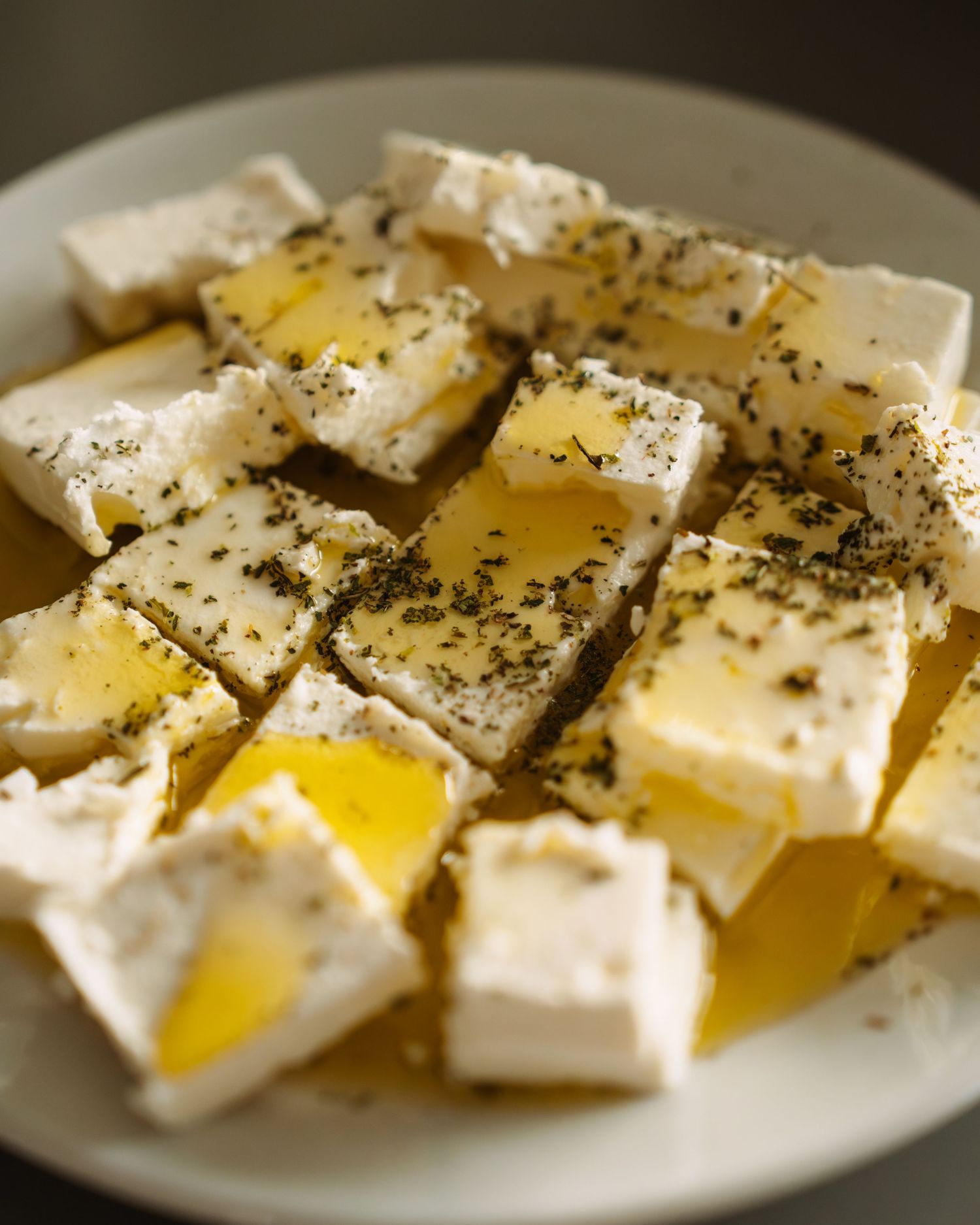Fresh mozzarella cheese slices drizzled with olive oil and seasoned with cracked black pepper on a white plate.