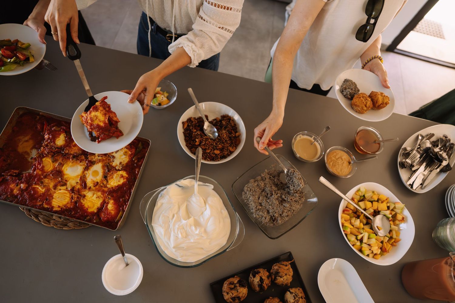 Hands serving and sharing various dishes at a dinner gathering around a wooden table.